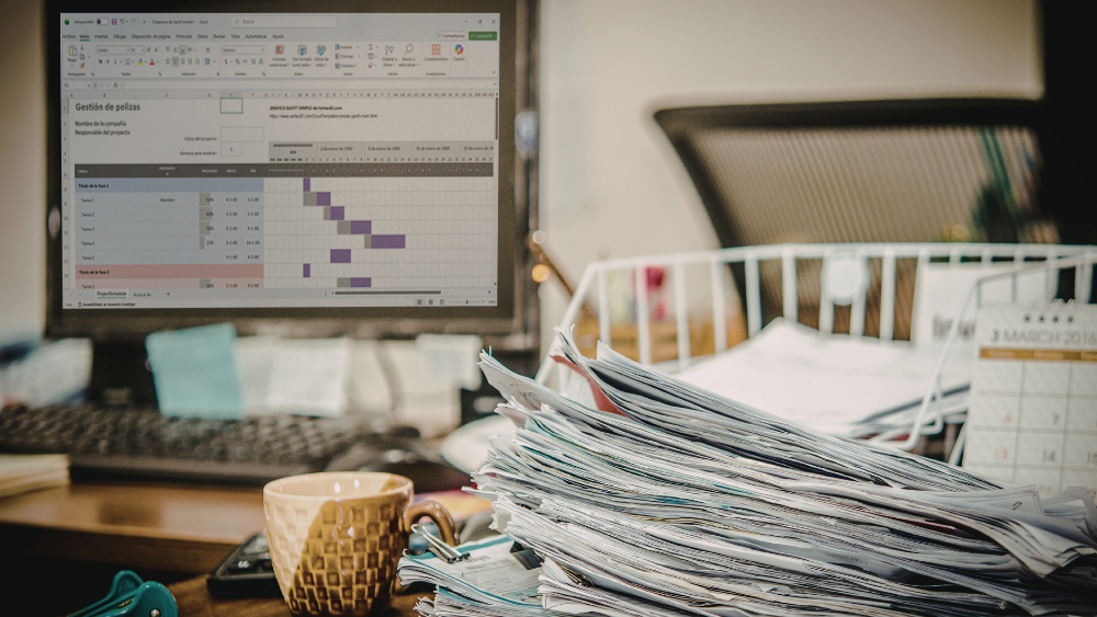 Escritorio desordenado con documentos y pantalla de Excel reflejando mala gestión de cartera de seguros